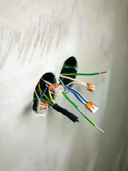 Colour-coded wires with orange push-in connectors coming out of a wall hole