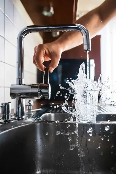 Chrome kitchen faucet filling a glass with water splashing